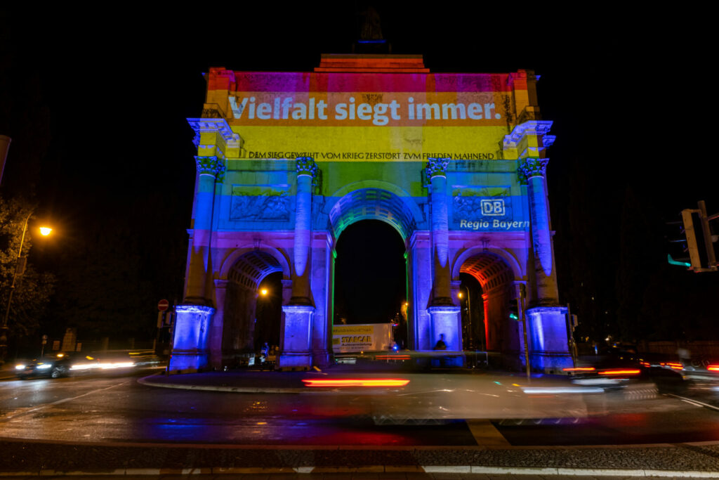 Das Siegestor in der Münchner Ludwigstraße ist in Regenbogenfarben erleuchtet. Der Schriftzug "Vielfalt gewinnt immer" ist zu lesen.