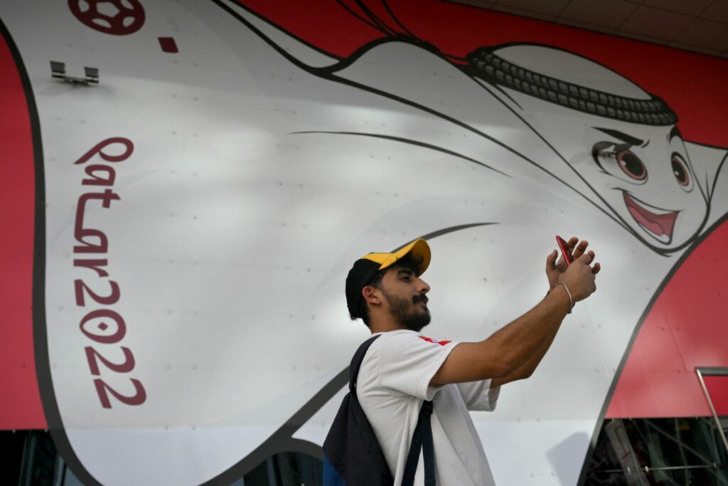 Mann mit Handy vor dem Logo der Wm 2022