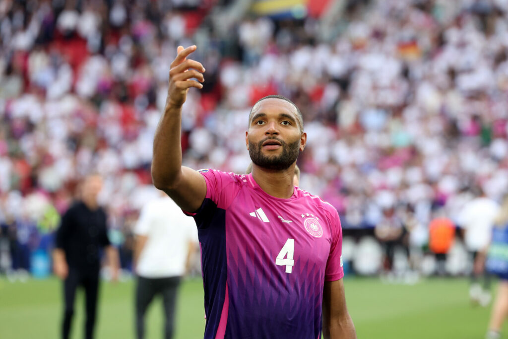Jonathan Tah hebt im pinken Trikot der deutschen Nationalmannschaft seine rechte Hand.
