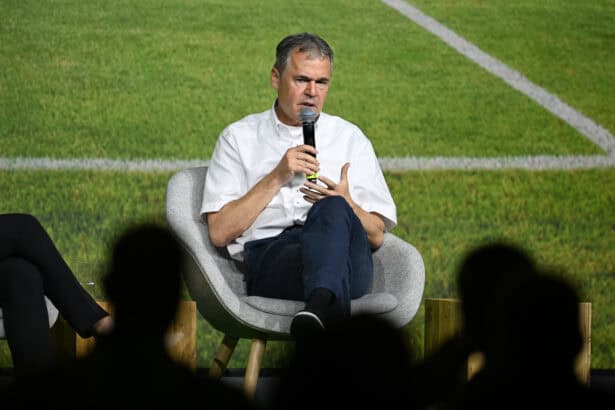 Andreas Rettig sitzt mit einem Mikrofon auf einer Bühne