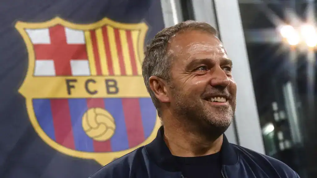 Hansi Flick smiling in front of the FC Barcelona crest
