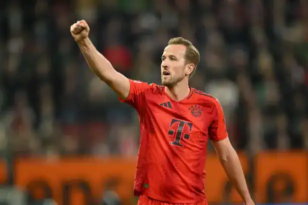 Harry Kane in a red FC Bayern Munich kit celebrating with a raised fist on the pitch.
