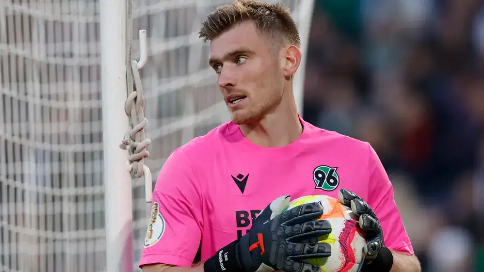 Hannover 96 goalkeeper Leo Weinkauf in a pink jersey holding a soccer ball in front of the goal net.