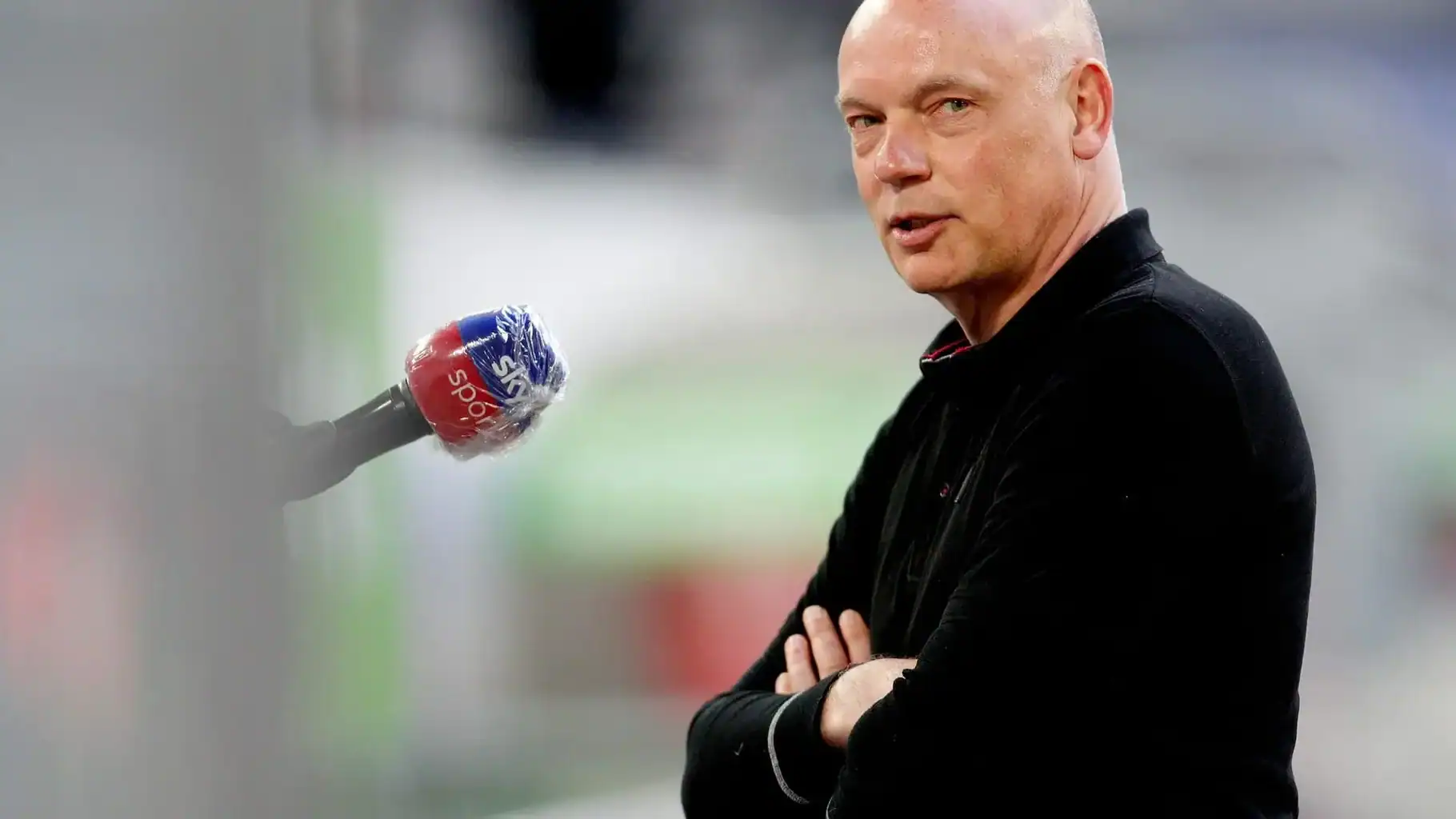 Portrait of Uwe Rösler in a black shirt with arms crossed during an interview