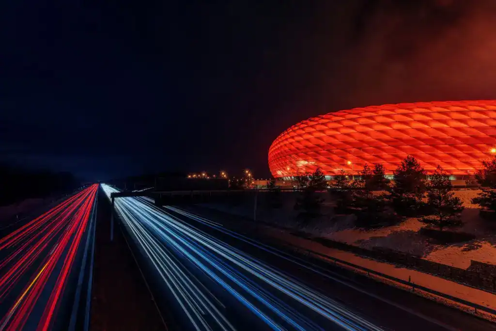 Night view of the Allianz Arena in Munich with its glowing red exterior and light trails from a highway