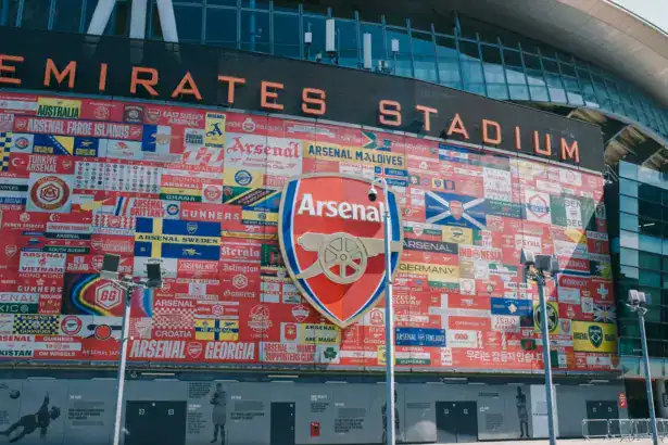 Exterior wall of Emirates Stadium featuring a large Arsenal FC crest surrounded by international fan flags